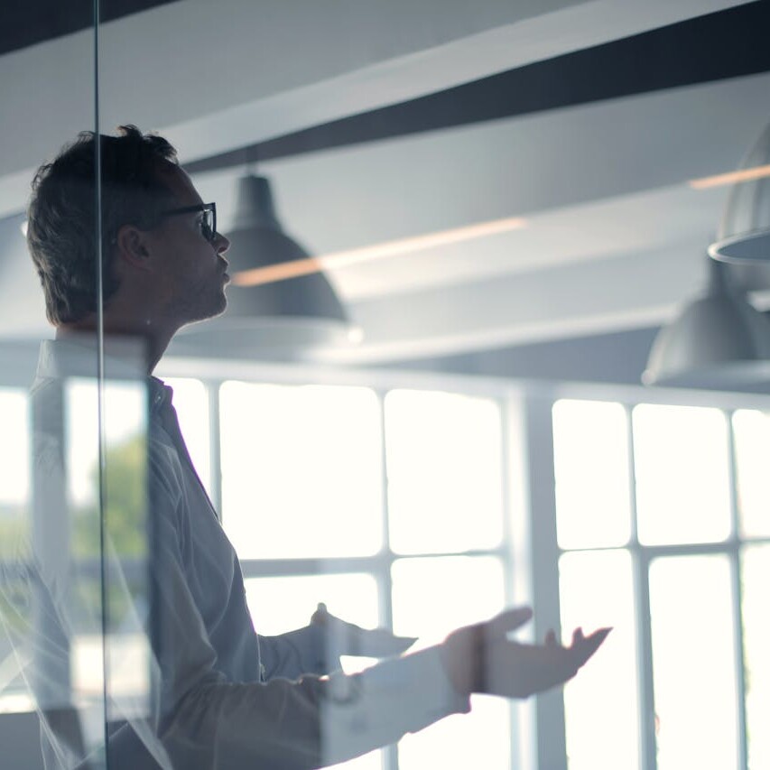 Businessman speaking in a glass-walled meeting room, delivering a professional presentation