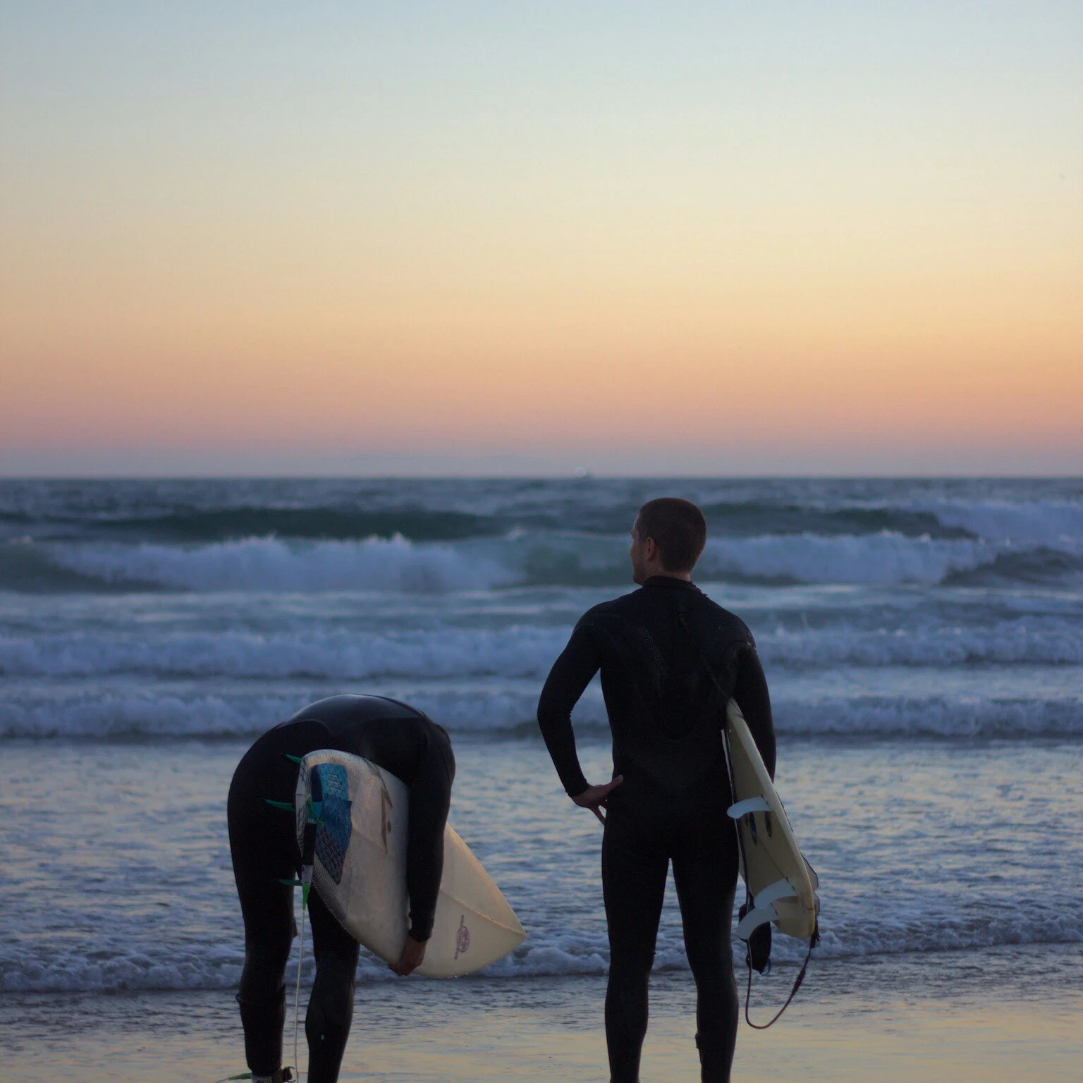 Two surfers standing on the beach looking at the ocean, representing strategic vision and partnership